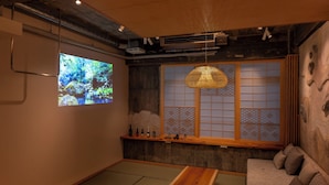 A traditional Japanese room with tatami flooring, a low wooden table, a cushioned sofa, a large shoji screen window, and a projector displaying a nature scene. - Walking distance from Asakusa, Japanese modern in Asakusa｜ 1 floor for private use｜ Ideal for couples and honeymooners｜ 30 square meters｜ Max 4 people (Matsugaya, Taito City)