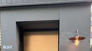 A modern building entrance with a metallic door, a small wooden sign, and a light fixture above the door. - Walking distance from Asakusa, Japanese modern in Asakusa｜ 1 floor for private use｜ Ideal for couples and honeymooners｜ 30 square meters｜ Max 4 people (Matsugaya, Taito City)