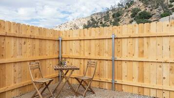A wooden fence with a table and two chairs in a gravel area.