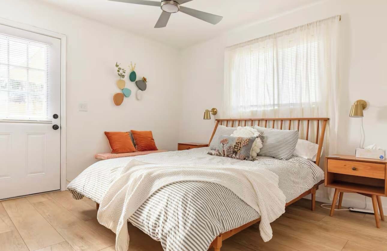 Ein Schlafzimmer mit einem Bett, Nachttischen, einem Deckenventilator, einem Fenster mit Vorhängen und Wanddekoration.
