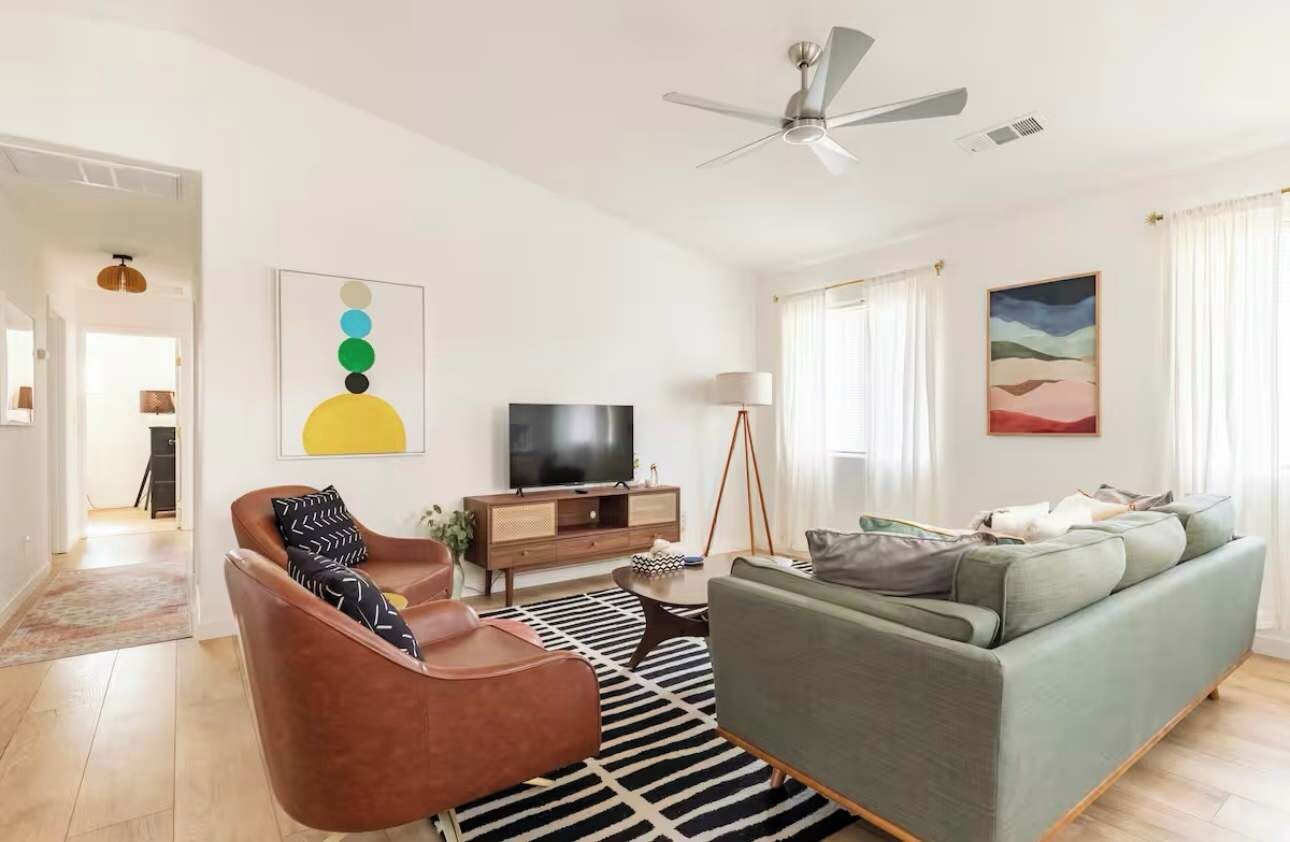 Un salon moderne avec un canapé, un fauteuil marron, un téléviseur et des œuvres d’art accrochées aux murs.