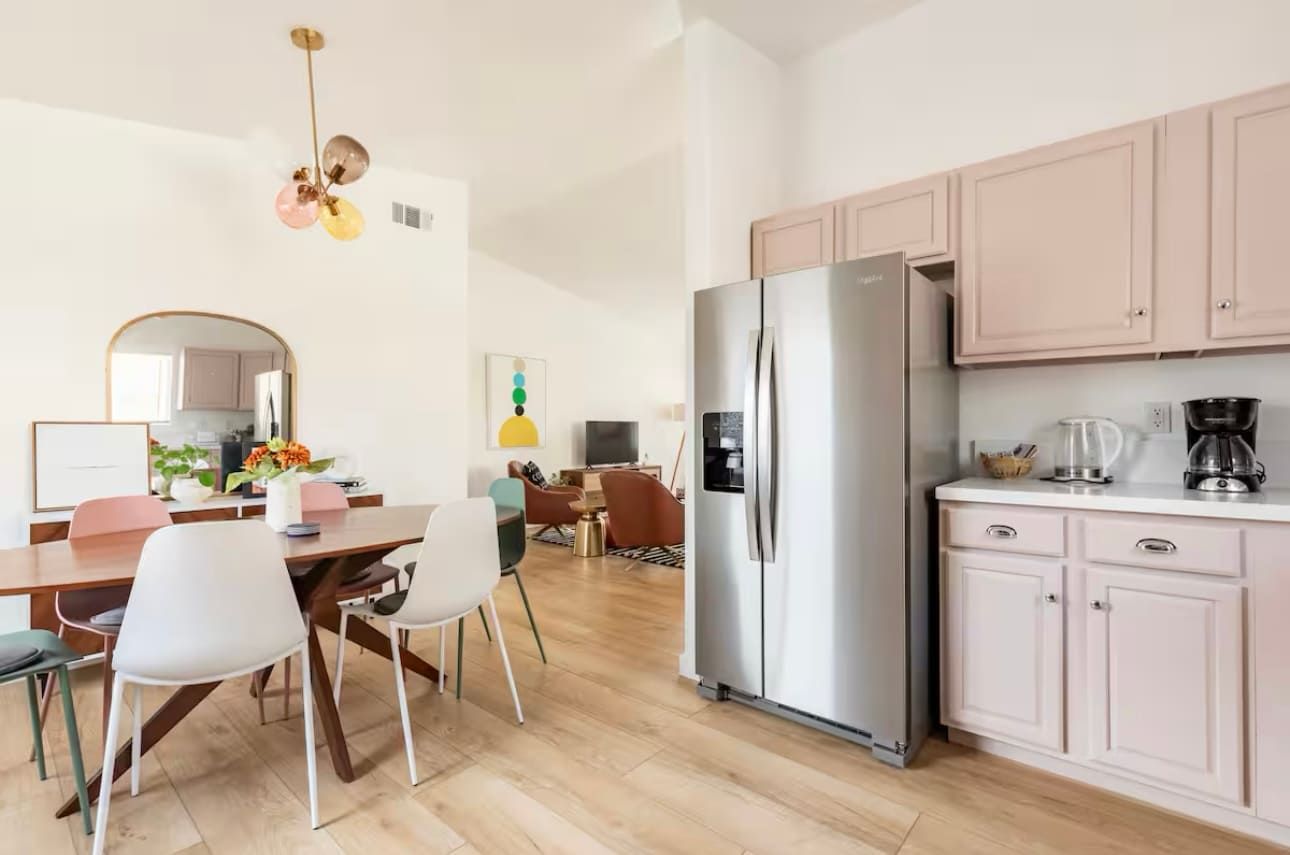 A modern kitchen with a stainless steel refrigerator, wooden cabinets, and a dining area with a table and chairs.