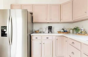 A kitchen with light pink cabinets, a stainless steel refrigerator, a coffee maker, and a kettle on the counter. - Kid-Ready Retreat: Lake Isabella Fun (Lake Isabella)