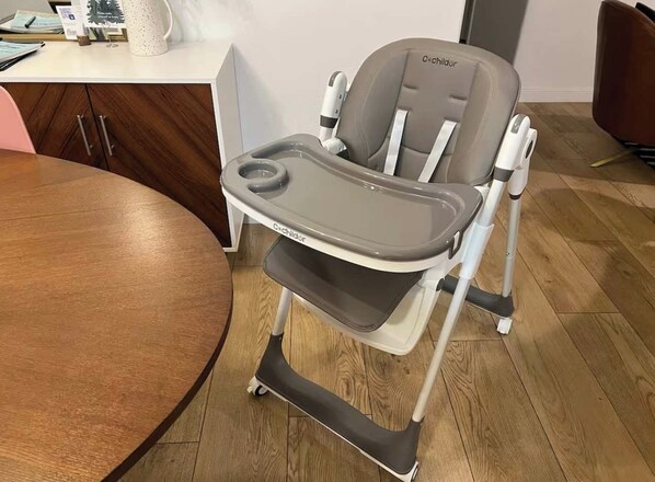 Une chaise haute dotée d’un plateau et d’un repose-pieds, placée dans une pièce dont le sol est recouvert de parquet et qui contient une table ronde.