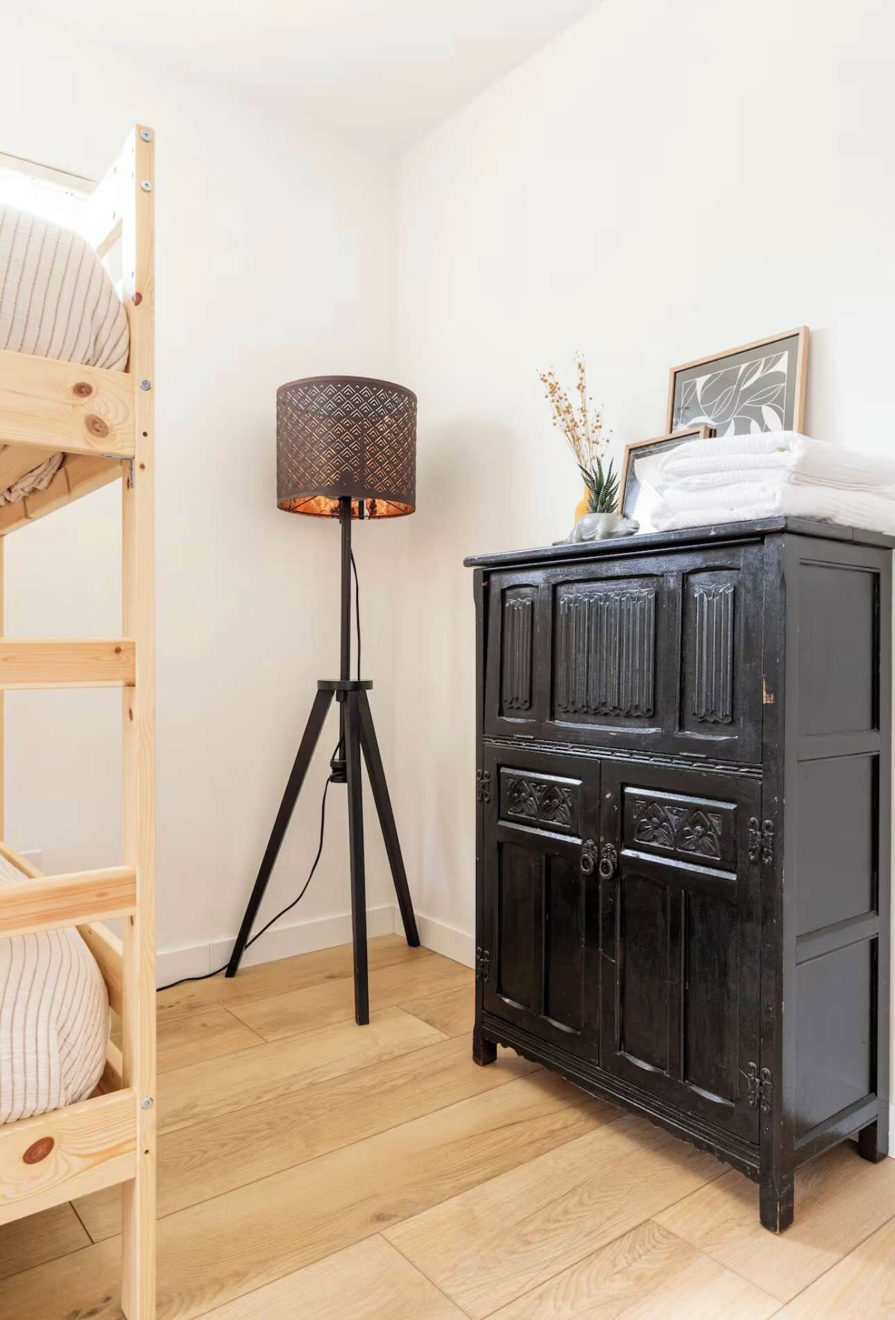 A room with a wooden bunk bed, a black cabinet with decorative carvings, and a floor lamp with a patterned lampshade.