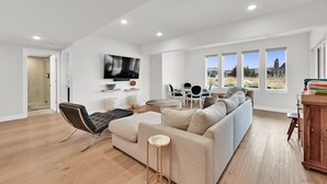 Ein modernes Wohnzimmer mit einer Couch, Sesseln, einem Fernseher und Blick ins Freie.