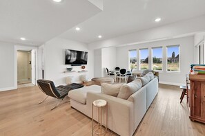 A modern living room with a sofa, chairs, a TV, and a view of the outdoors. - Eden Mountain Oasis: Hot Tub & Stunning Views (Eden)