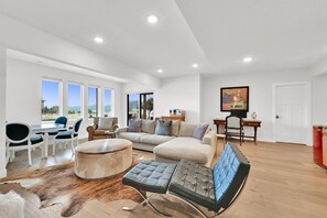 A spacious living area with a large sofa, a round ottoman, and a leather chair. There are multiple windows offering a view of the outdoors. - 5 Bed 5 Bath Mountain Oasis with Private Hot Tub (Eden)