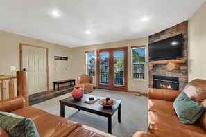 Ein Wohnzimmer mit Ledersofas, einem Couchtisch, einem Kamin und einem an einer Steinwand montierten Fernseher.