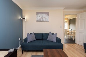 Un salón con un sofá azul oscuro, una mesa de centro de madera y una lámpara de pie.