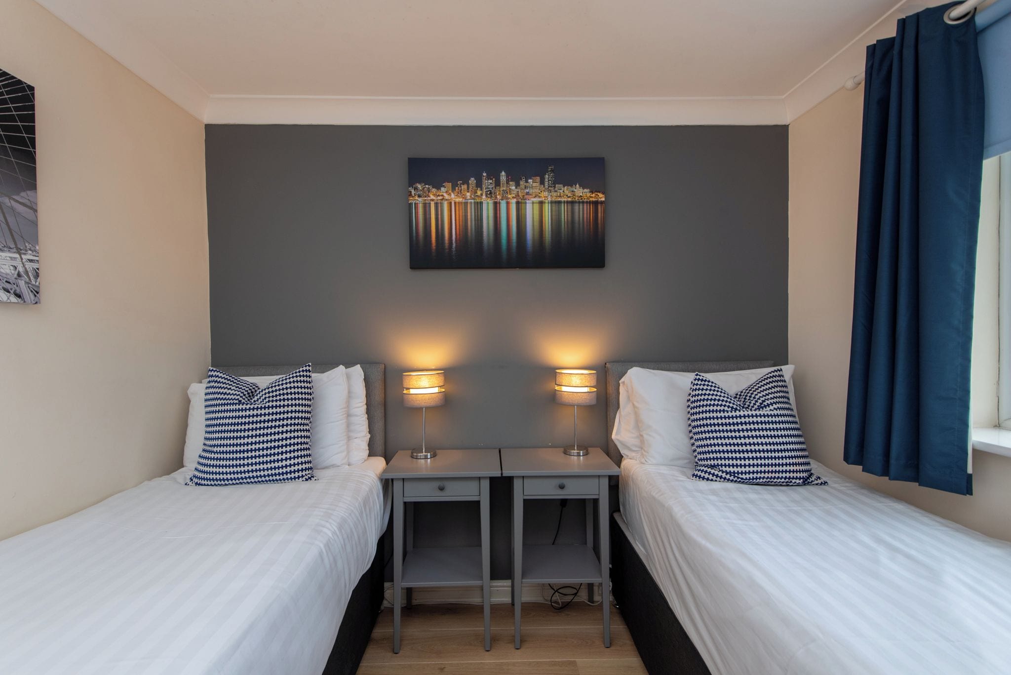 Een hotelkamer met twee bedden, een bureau en een stadsgezichtschilderij aan de muur.
