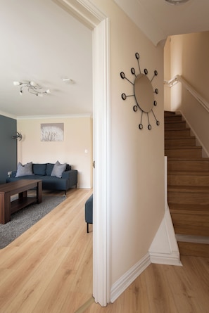 A modern living room with a wooden floor, a dark blue sofa, a wooden coffee table, and a unique wall clock. - Toast Stays - Hillbrook (Thornaby)