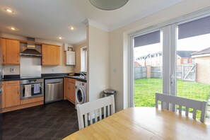 A modern kitchen with wooden cabinets, stainless steel appliances, and a dining area with a table and chairs. - Toast Stays - Hillbrook (Thornaby)