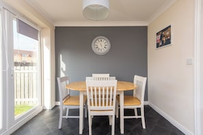 A dining area with a round table and four white chairs, a wall clock, and a bulletin board with various notices. - Toast Stays - Hillbrook (Thornaby)
