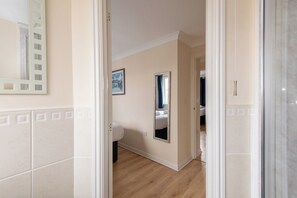A hallway with a bathroom visible in the background, featuring a toilet, sink, and mirror. - Toast Stays - Hillbrook (Thornaby)