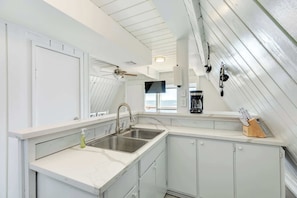 A kitchen with white cabinetry, a double sink, and a coffee maker. - Unique Beachfront Escape Directly Over The Ocean (Surfside Beach)