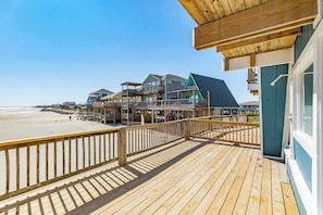 A wooden deck with a view of a beach and several buildings with balconies. - Unique Beachfront Escape Directly Over The Ocean (Surfside Beach)