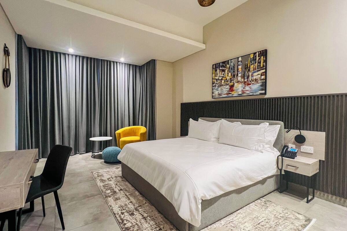 Ein modernes Hotelzimmer mit einem großen Bett, einem Schreibtisch, einem Sessel und einem kleinen runden Tisch.