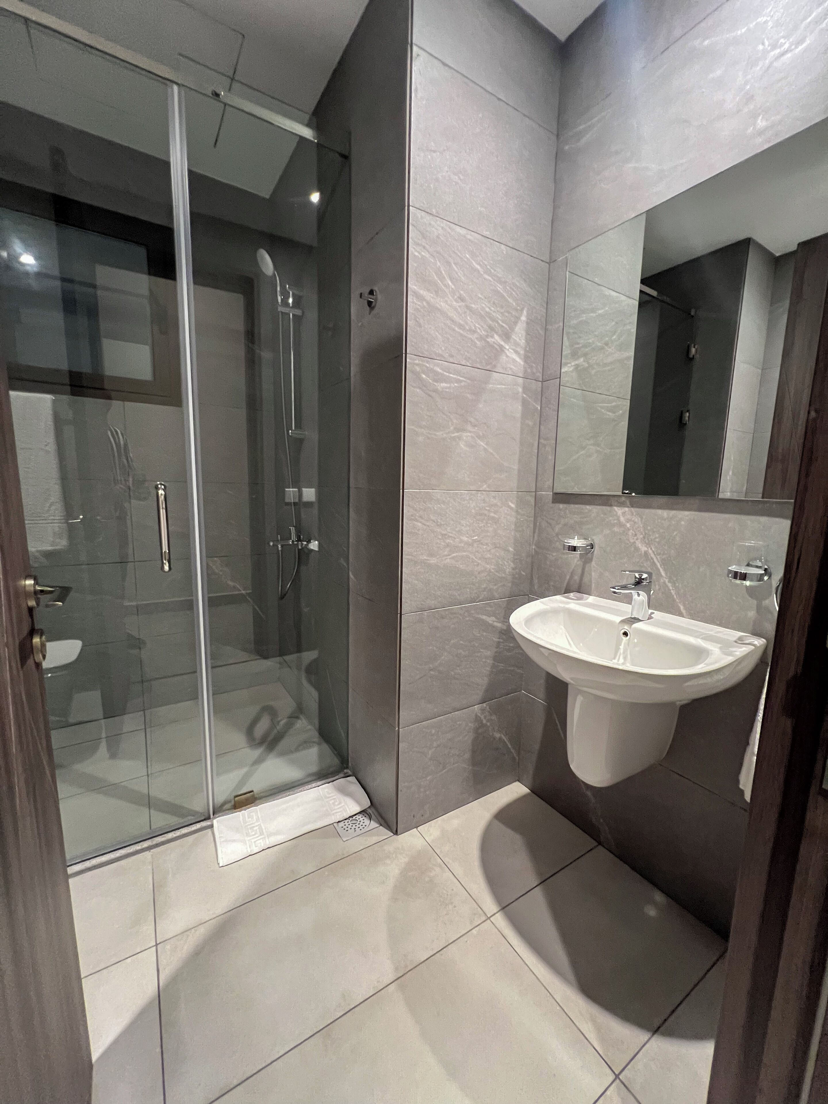 A modern bathroom with a glass shower enclosure, a sink, and a mirror.