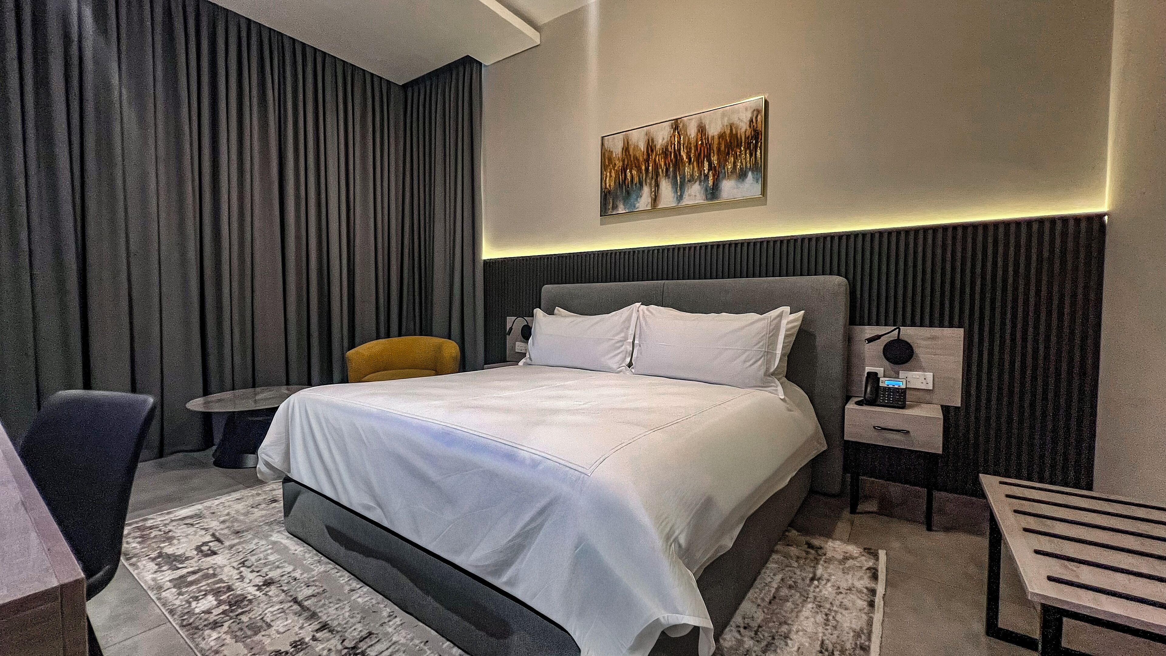 A modern hotel room with a large bed, a small table, a chair, and a nightstand with a phone.