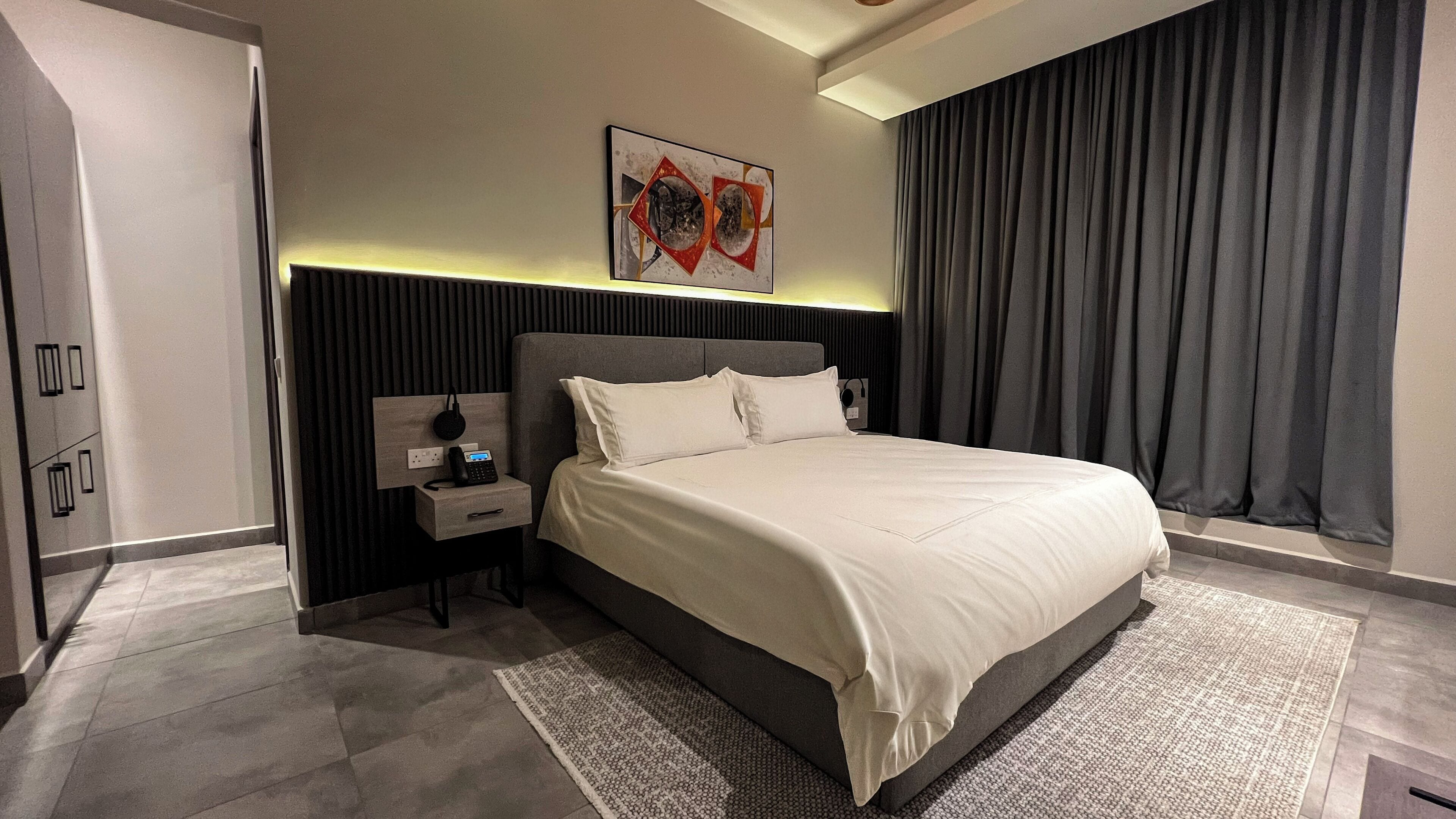 Un dormitorio moderno con una cama grande, una mesita de noche con un teléfono y una obra de arte colgada en la pared.