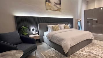 Un dormitorio moderno con una cama grande, un sofá gris, una mesita de noche, una lámpara de pared y un armario.