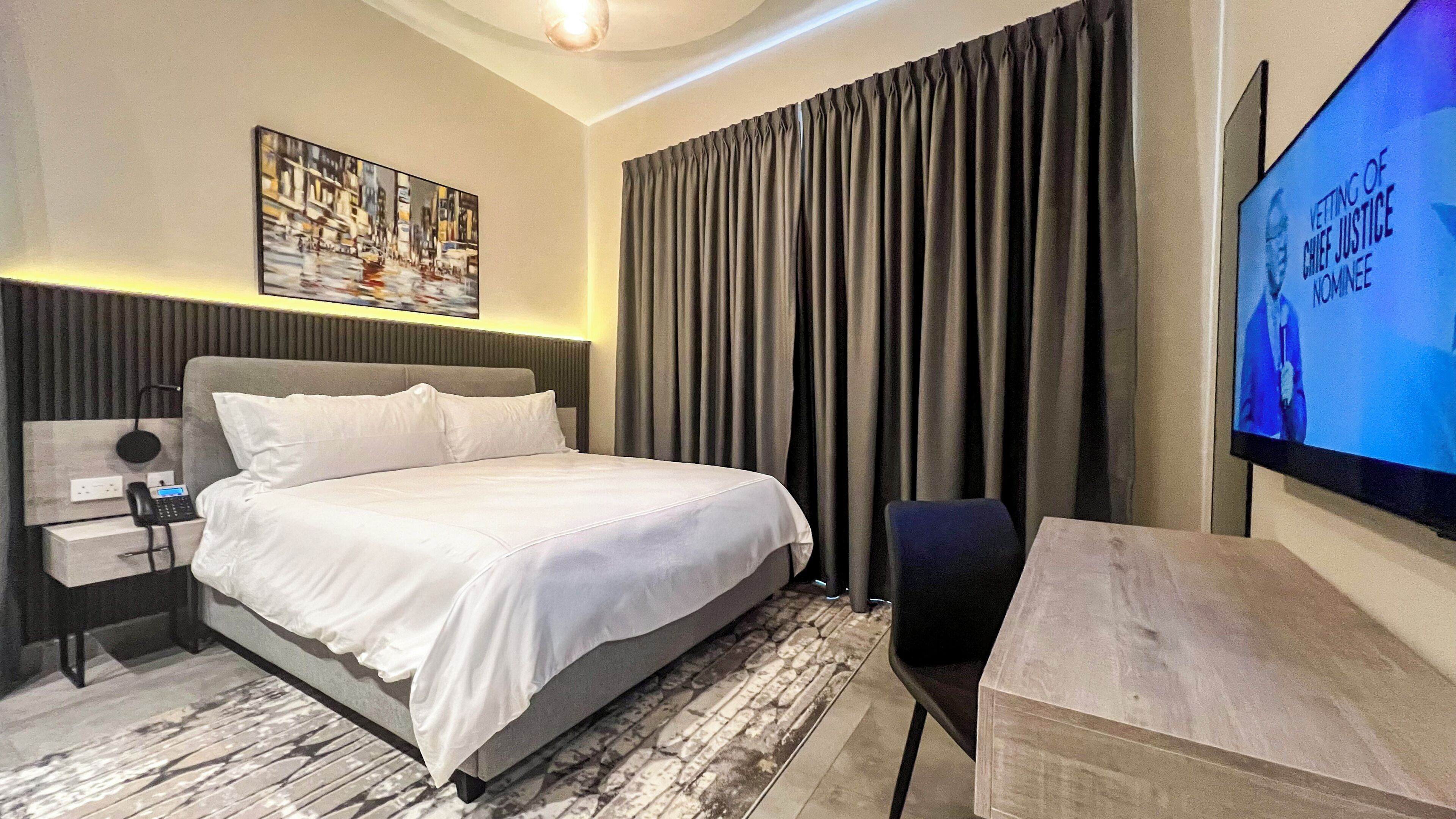 A hotel room with a large bed, a desk, a chair, a TV, and a painting on the wall.