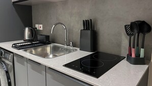 A modern kitchen with a stainless steel sink, a kettle, a built-in stovetop, and a knife block. - Anthonian Suites (Accra)