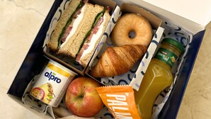 Una fiambrera con sándwiches, un croissant, una manzana, una botella de jugo, un envase de yogur y una bolsita de snack.