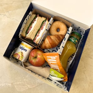 Una fiambrera con sándwiches, un croissant, una manzana, una botella de jugo, un envase de yogur y una bolsita de snack.