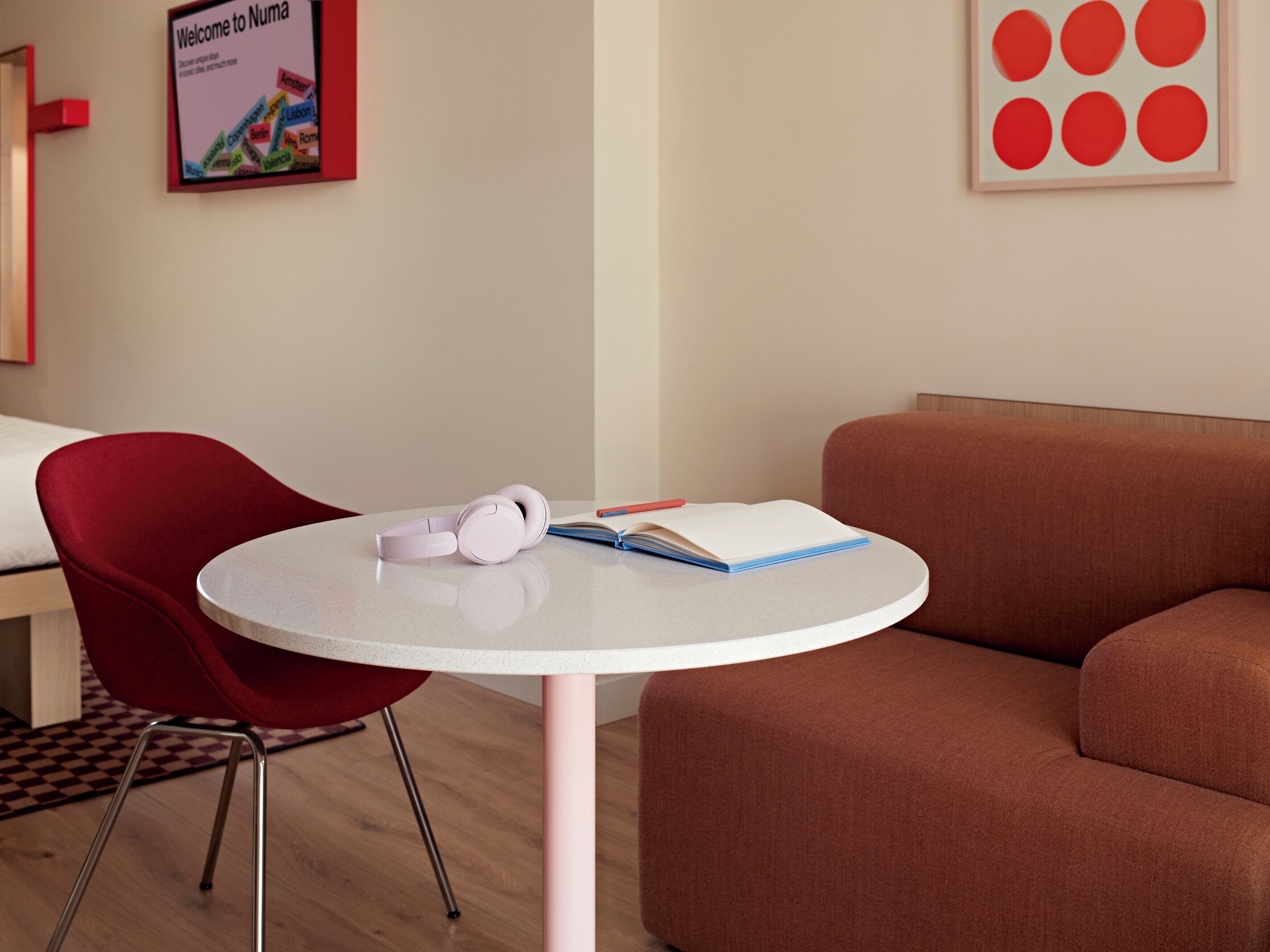 A modern room with a round table, a red chair, a sofa, and a poster on the wall.