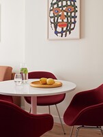 A dining area with a round table, red chairs, a plate with lemons, a glass of water, and a bottle of water.