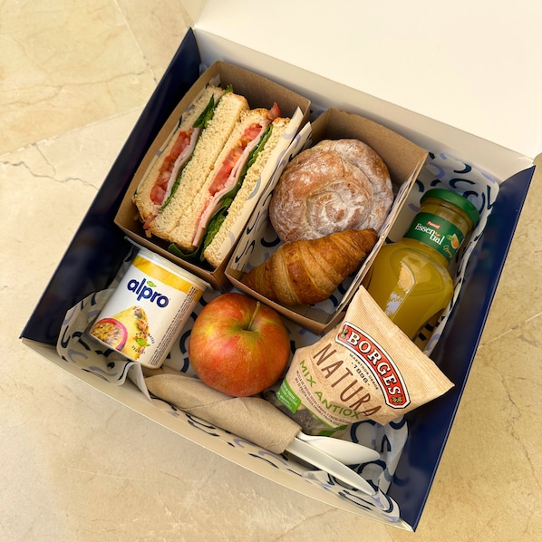 Una fiambrera con sándwiches, un croissant, una manzana, una botella de jugo, un envase de yogur y una bolsa de pan.