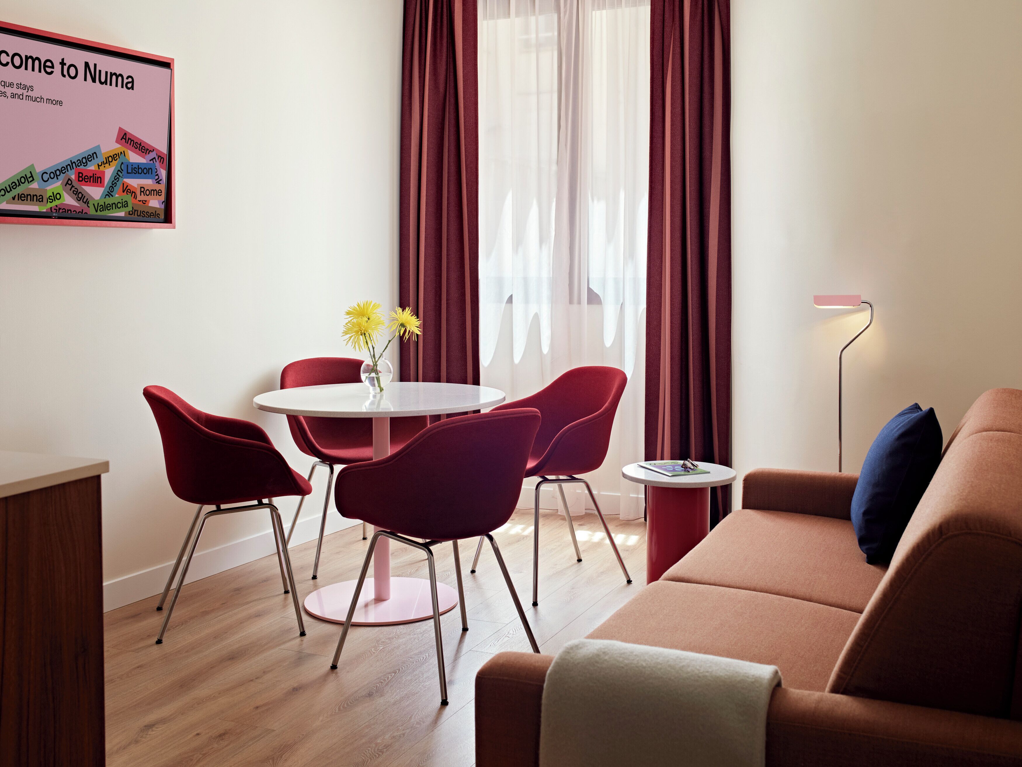 A modern living room with a round dining table, red chairs, a sofa, and a floor lamp.