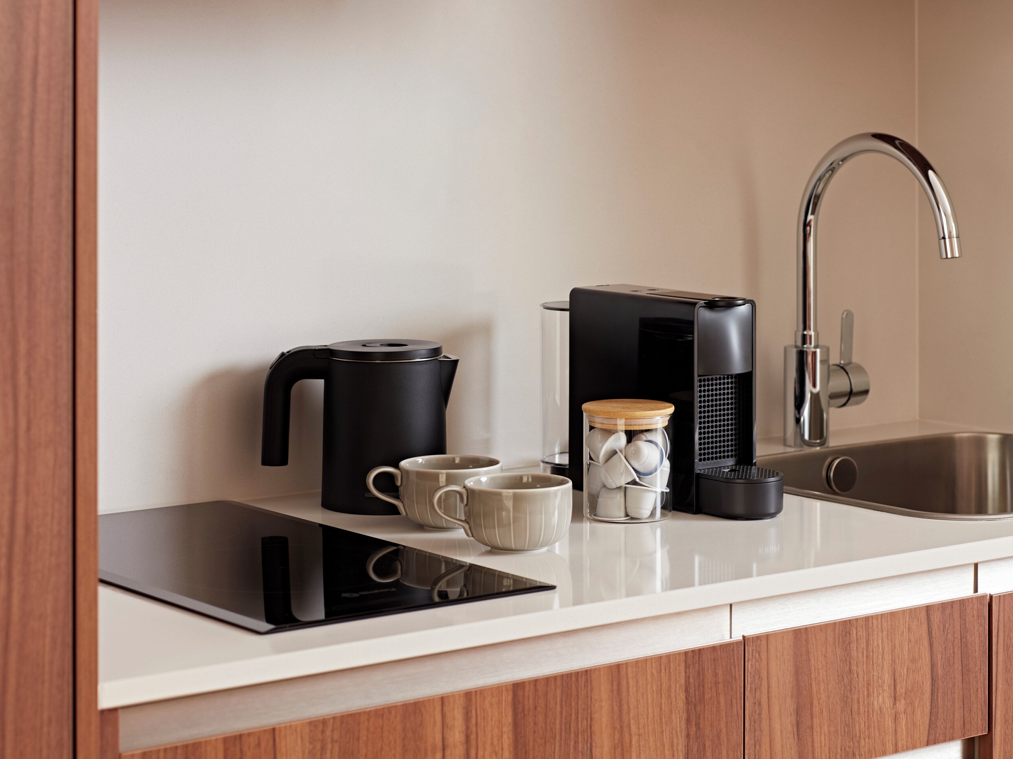 A modern kitchen with a black coffee maker, a kettle, a toaster, a coffee machine, and a stainless steel sink.