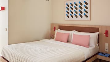 A neatly made bed with a white quilt and pink pillows, a wooden headboard, a wall-mounted light fixture, and a framed picture above the bed.