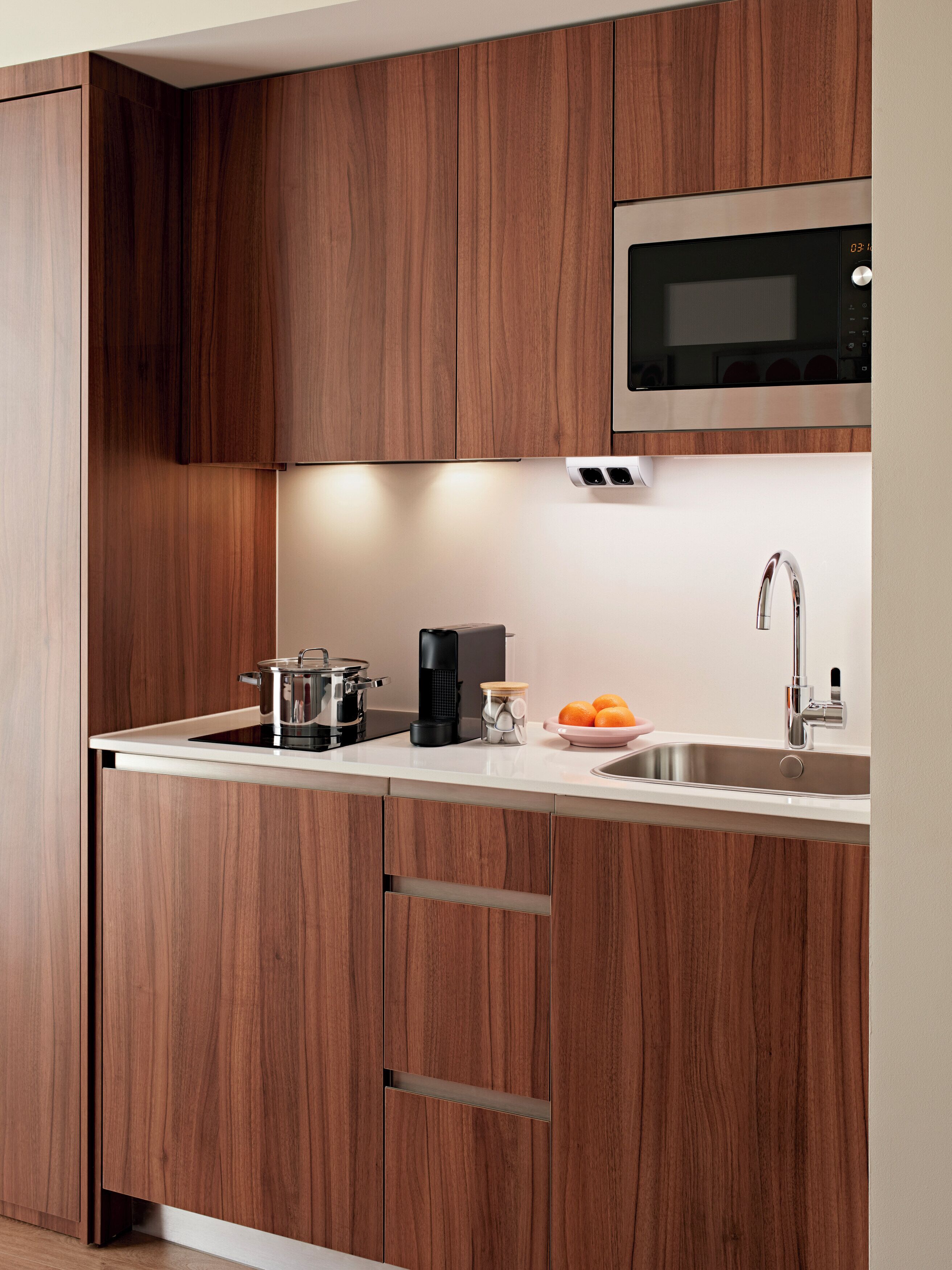 Una cocina moderna con armarios de madera, un lavamanos de acero inoxidable, un microondas y una cafetera.