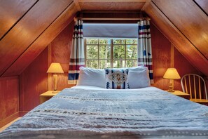 Ein gemütliches Schlafzimmer im Dachgeschoss mit einem großen Bett, zwei Nachttischlampen und einem Fenster mit Vorhängen.