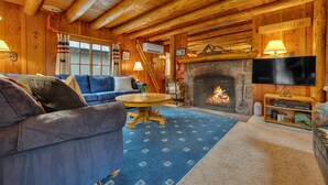 Ein gemütliches Blockhaus-Interieur mit Kamin, Fernseher und einem blauen Teppich mit Muster.
