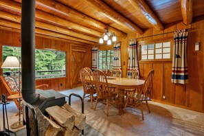A wooden interior with a round dining table, chairs, a fireplace, and large windows. - Berghuttlein Getaway - Cozy family retreat w creek (Government Camp)