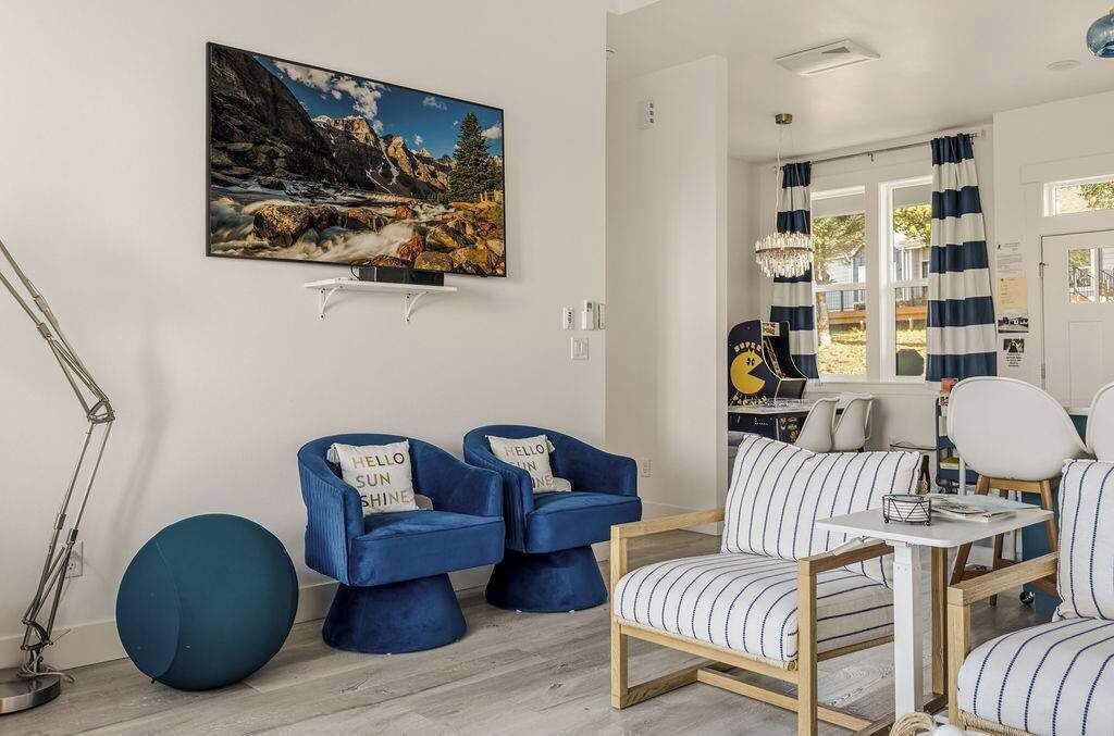 Uma sala de estar moderna com uma pintura de paisagem montanhosa, poltronas estofadas em azul, um sofá listrado e uma pequena mesa.