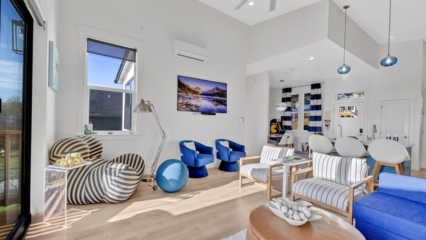 A modern living room with a large window, a flat-screen TV, and a variety of seating options including striped sofas and chairs.