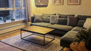 Ein gemütliches Wohnzimmer mit einem grünen Sofa, einem Holztisch und einer hängenden Leuchte.