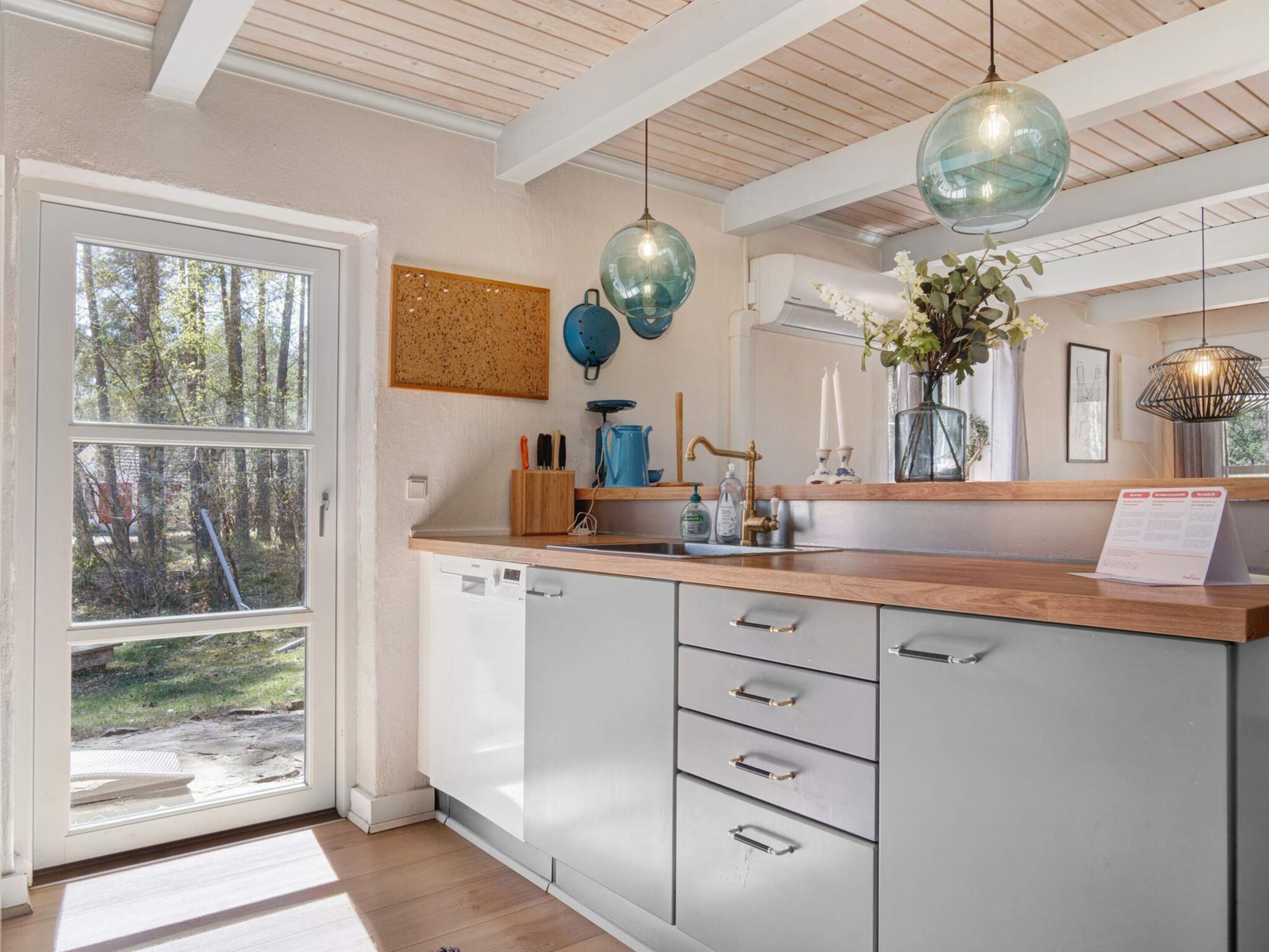 A modern kitchen with a wooden countertop, grey cabinets, and a large window.