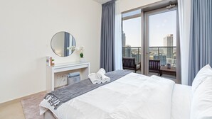 Ein modernes Hotelzimmer mit einem großen Bett, einem Schminktisch mit Spiegel und Blick auf die Stadt durch eine Schiebetür.