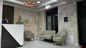 Ein Empfangsbereich mit einer Rezeption, zwei Sesseln, einer Chandelüster und einer Wand mit dekorativem Muster.