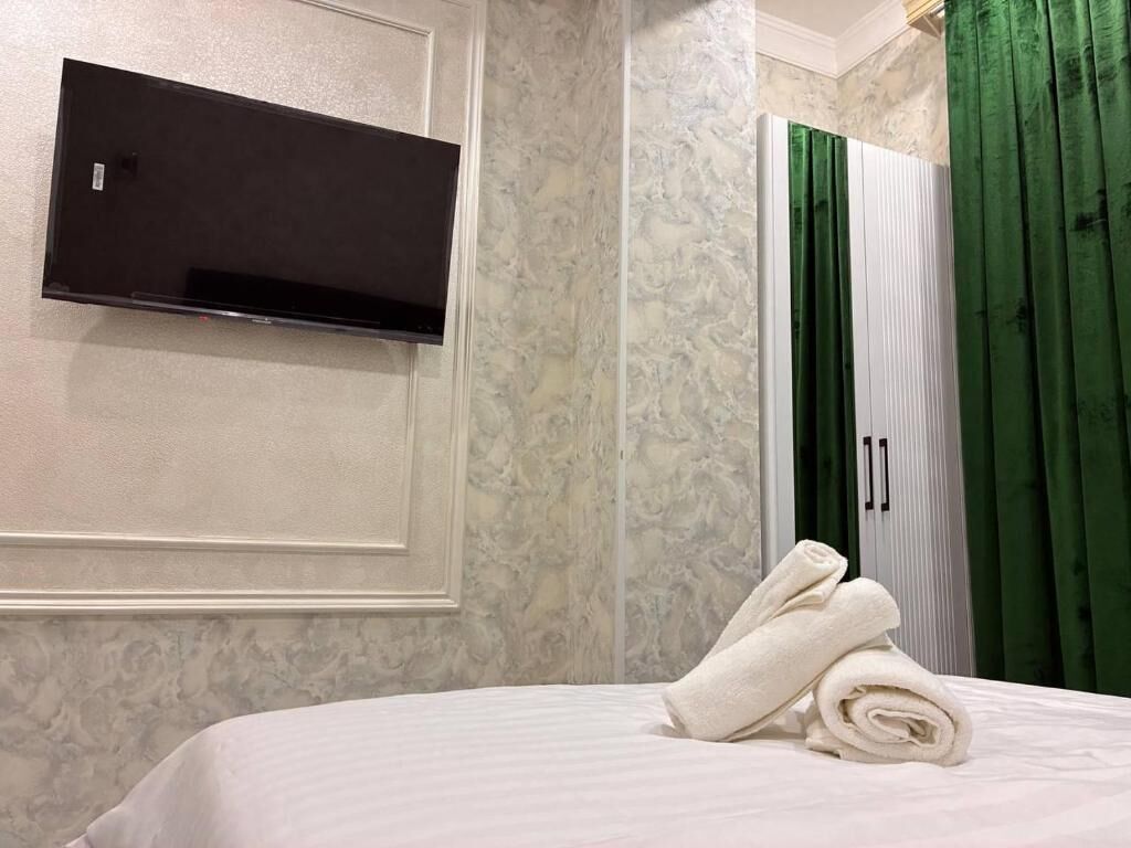 A hotel room with a bed, a flat-screen TV mounted on the wall, and a green curtain.