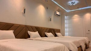 Ein Hotelzimmer mit zwei Betten, einem modernen Kopfteil, eingelassener Beleuchtung und einer Klimaanlage.