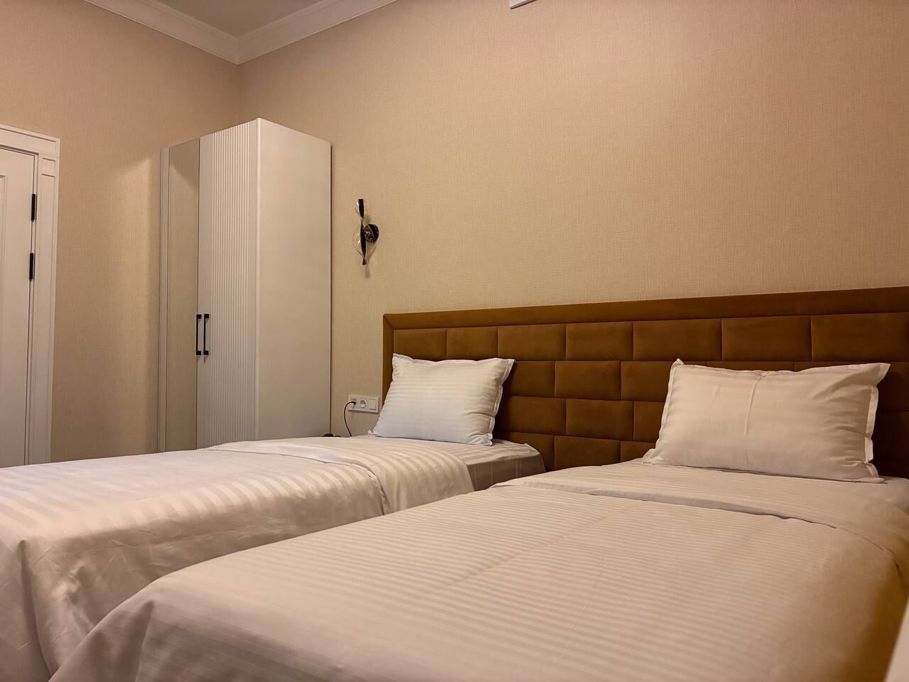 A hotel room with two single beds, a wardrobe, and a wall-mounted light fixture.