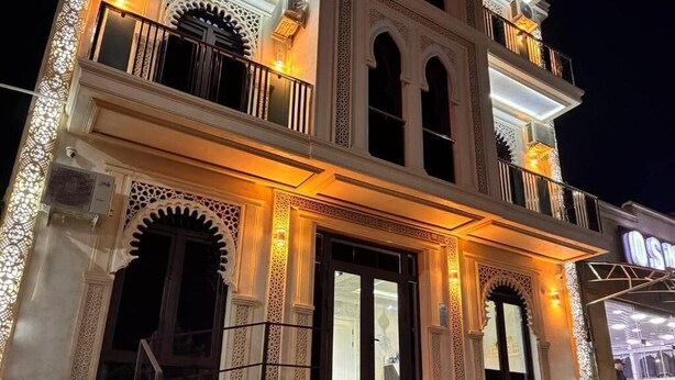 Ein zweistöckiges Gebäude mit aufwendigen architektonischen Details, darunter Bögen und Säulen, und einem roten Teppich, der zum Eingang führt.